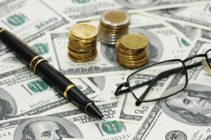 coins, pen and glasses over the hundred dollar bank notes